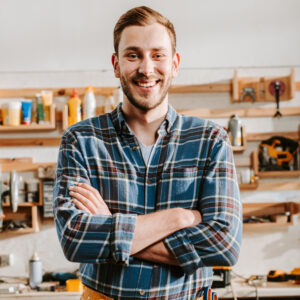 positive carpenter in apron standing with crossed arms